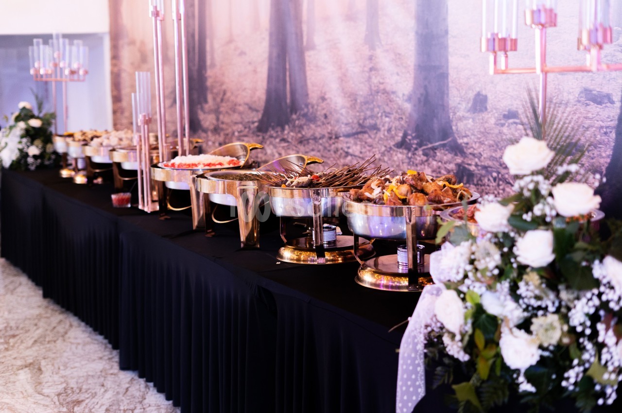 Buffet élégant avec plats variés disposés sur une table noire, décorée de fleurs blanches et chandeliers.