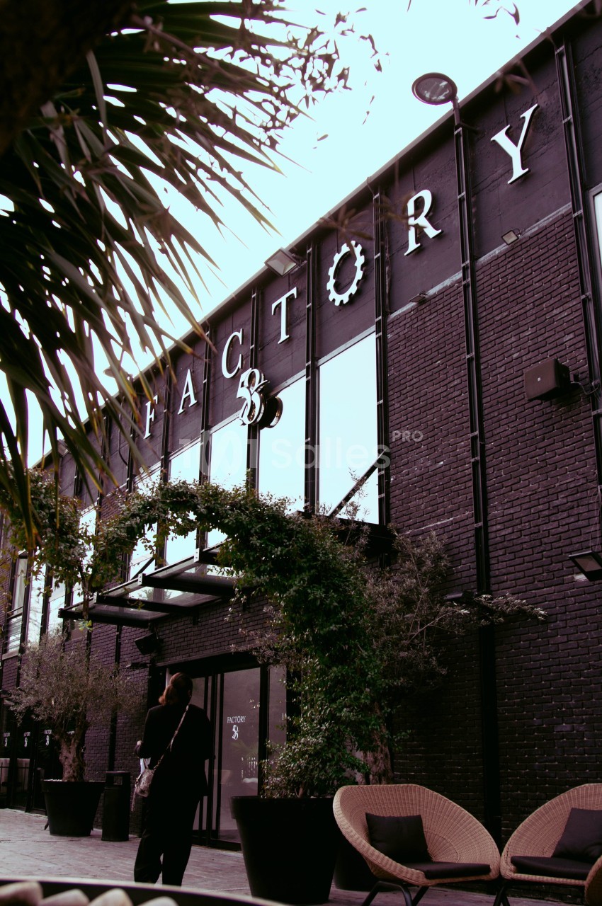 Façade en briques noires d'un bâtiment nommé ’Factory 58’, entourée de végétation et de mobilier extérieur.