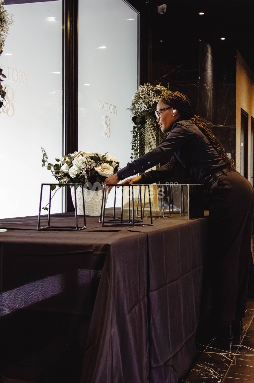 Une femme ajuste des décorations florales sur une table noire dans un espace intérieur élégant.
