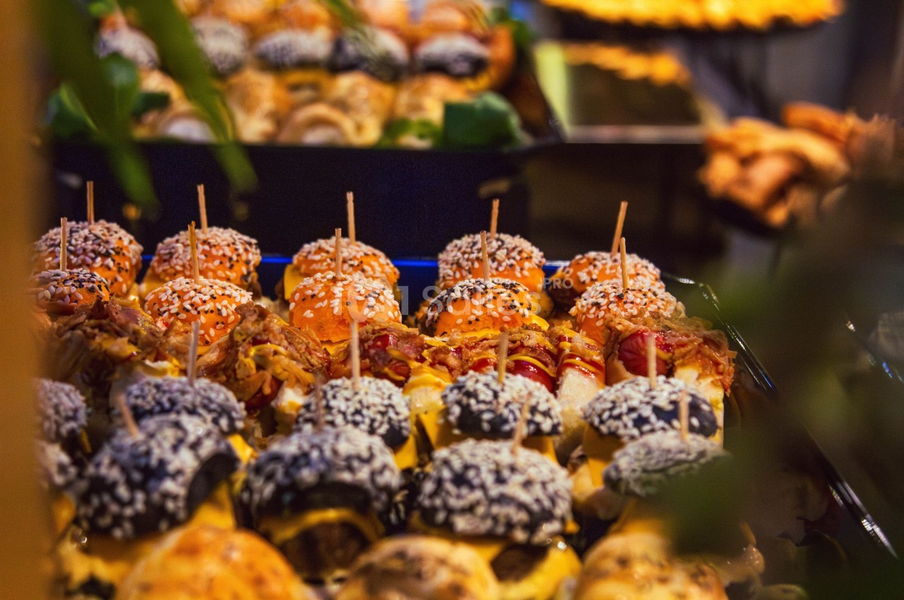 Plateau de mini-burgers variés garnis de graines de sésame, présentés sur une table lors d'un buffet.