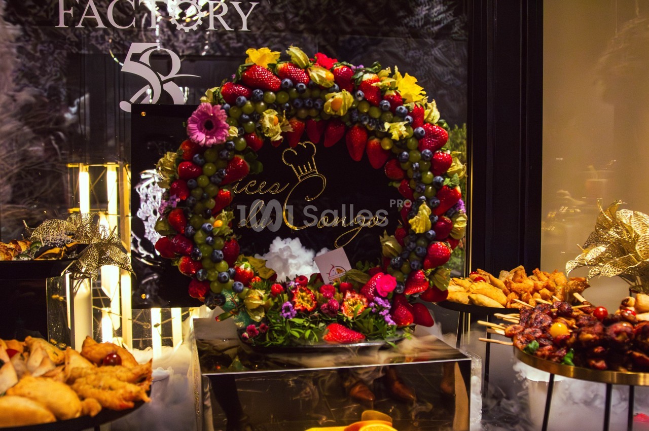 Couronne de fruits colorés avec fraises, myrtilles et fleurs, entourée de plats variés sur une table festive.