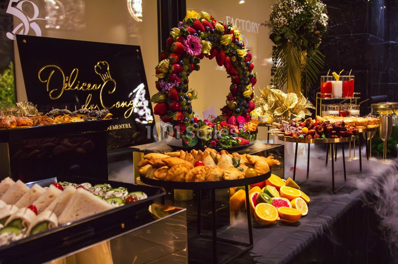 Buffet varié avec pâtisseries, fruits, sandwichs et décorations florales dans un cadre élégant.