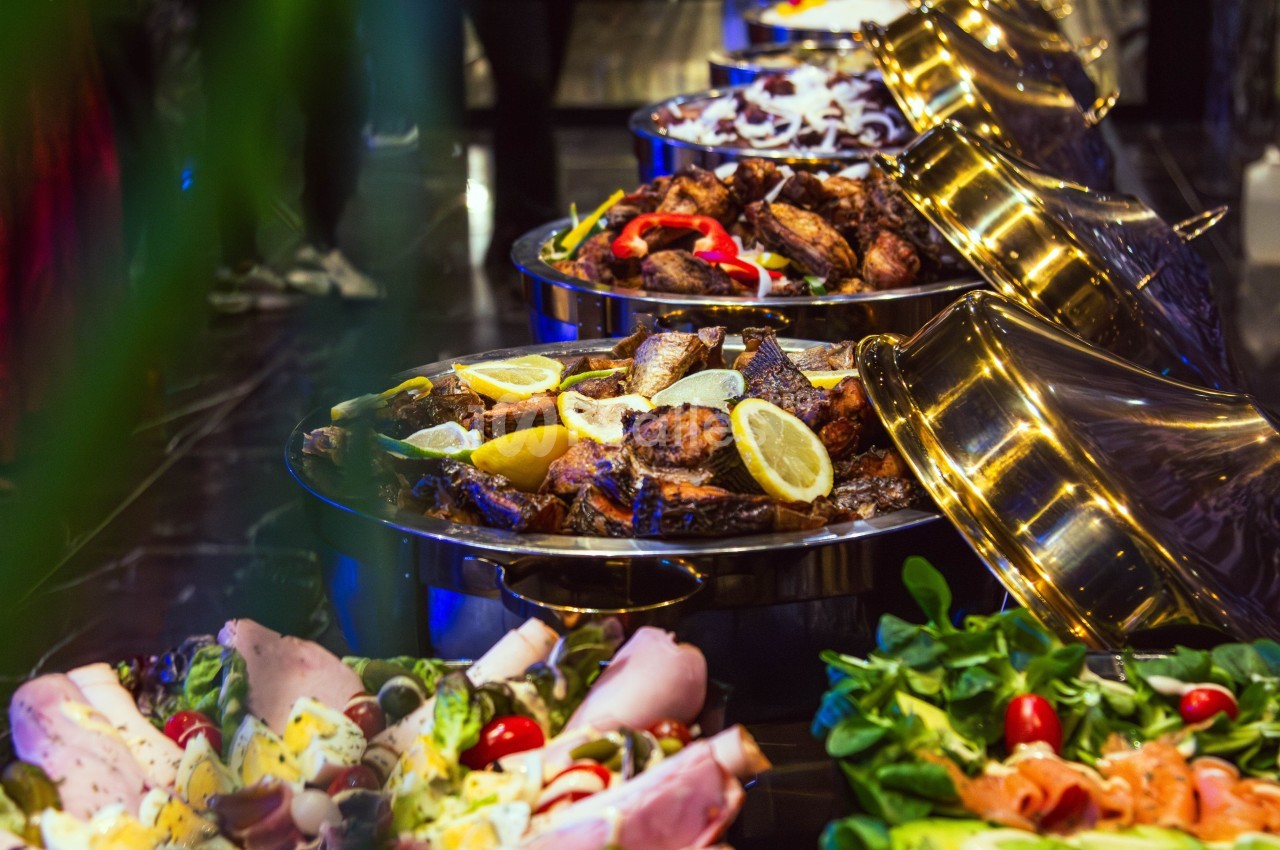 Buffet varié avec plats de viande grillée, légumes frais et charcuterie, présenté dans des plats en métal.