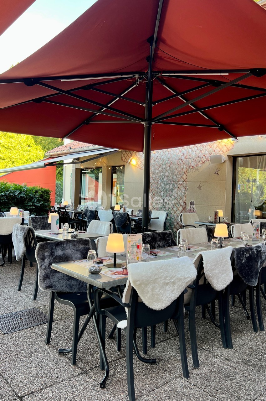 Terrasse d'un restaurant avec tables dressées, chaises couvertes de plaids et grands parasols rouges.