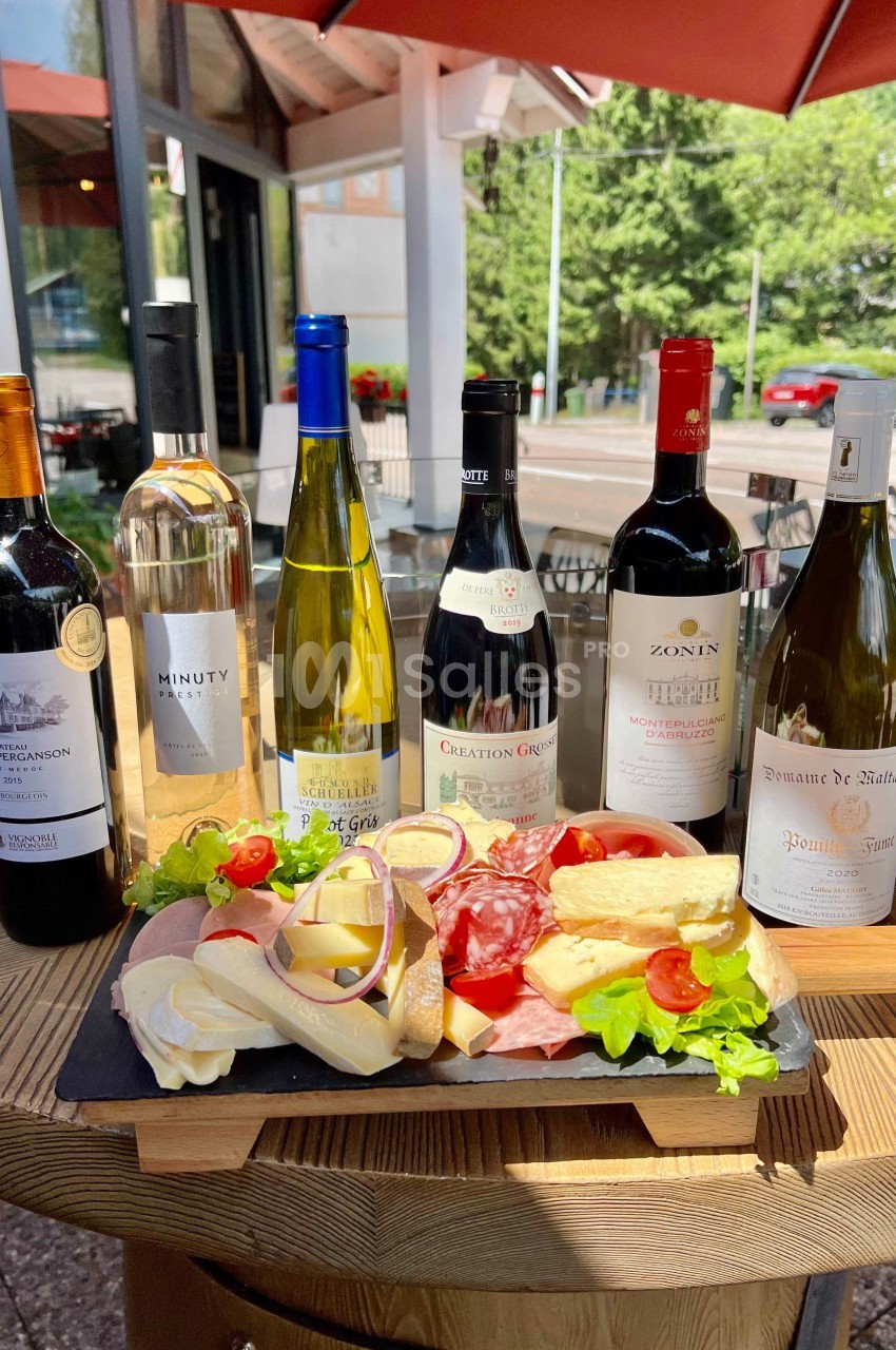 Plateau de charcuterie et fromages avec six bouteilles de vin disposés sur une table en terrasse.