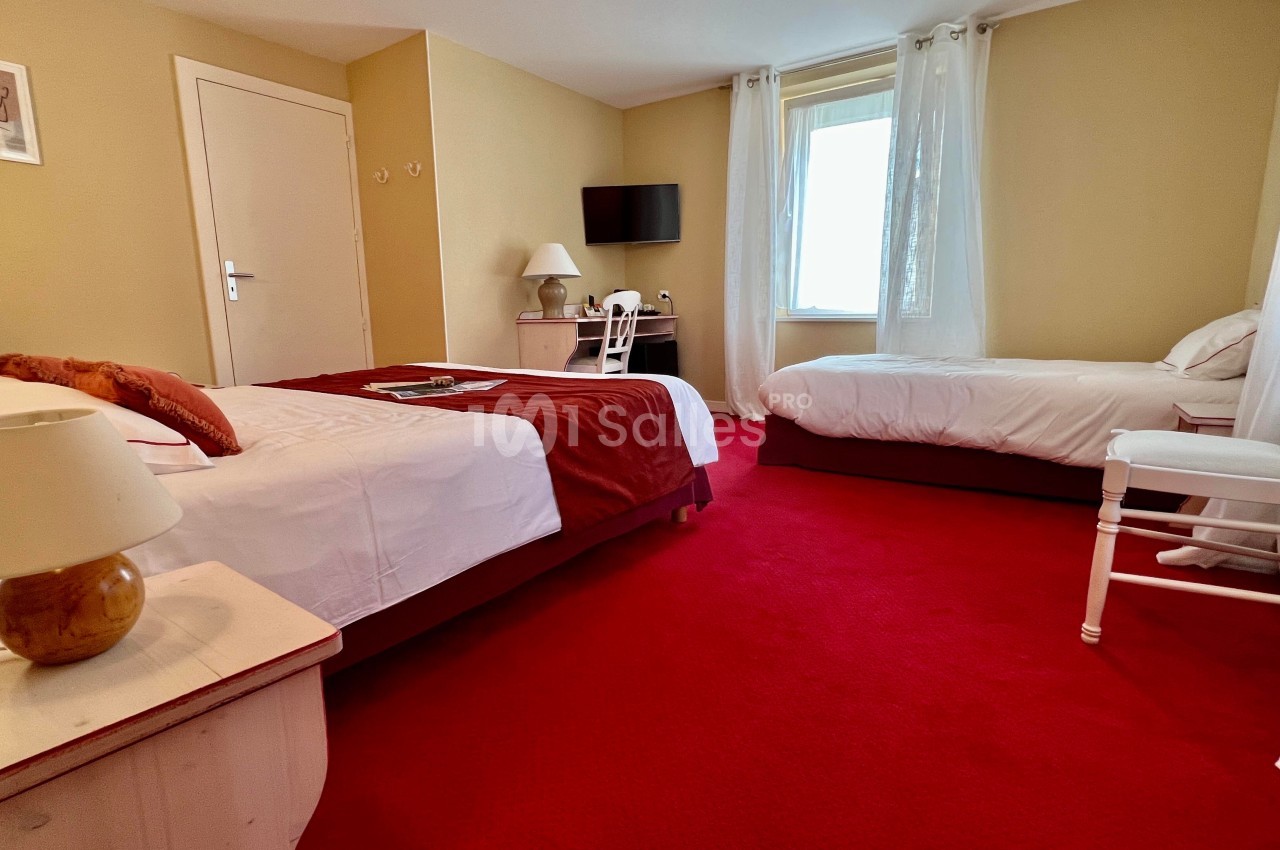 Chambre avec deux lits, moquette rouge, bureau, télévision murale et lumière naturelle provenant d'une fenêtre.