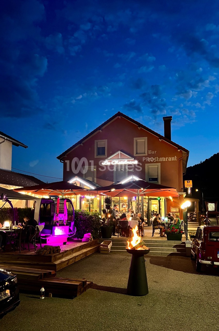 Terrasse d'un restaurant éclairée en soirée, avec des clients attablés et un brasero au premier plan.