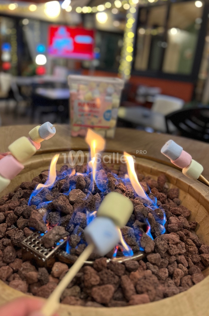 Des guimauves colorées sont grillées sur un feu de table entouré de pierres volcaniques dans un cadre convivial.