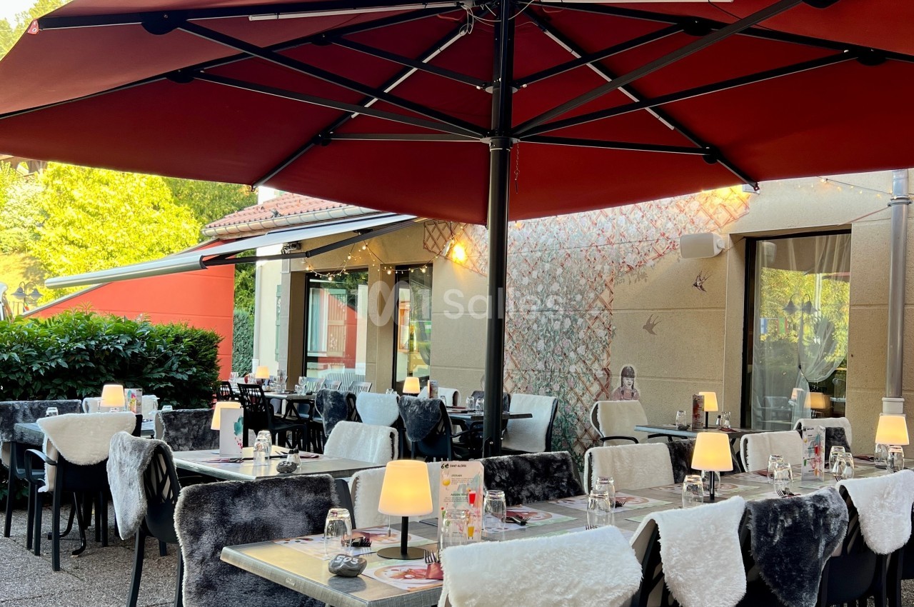 Terrasse de restaurant avec tables dressées, chaises couvertes de plaids et grands parasols rouges.