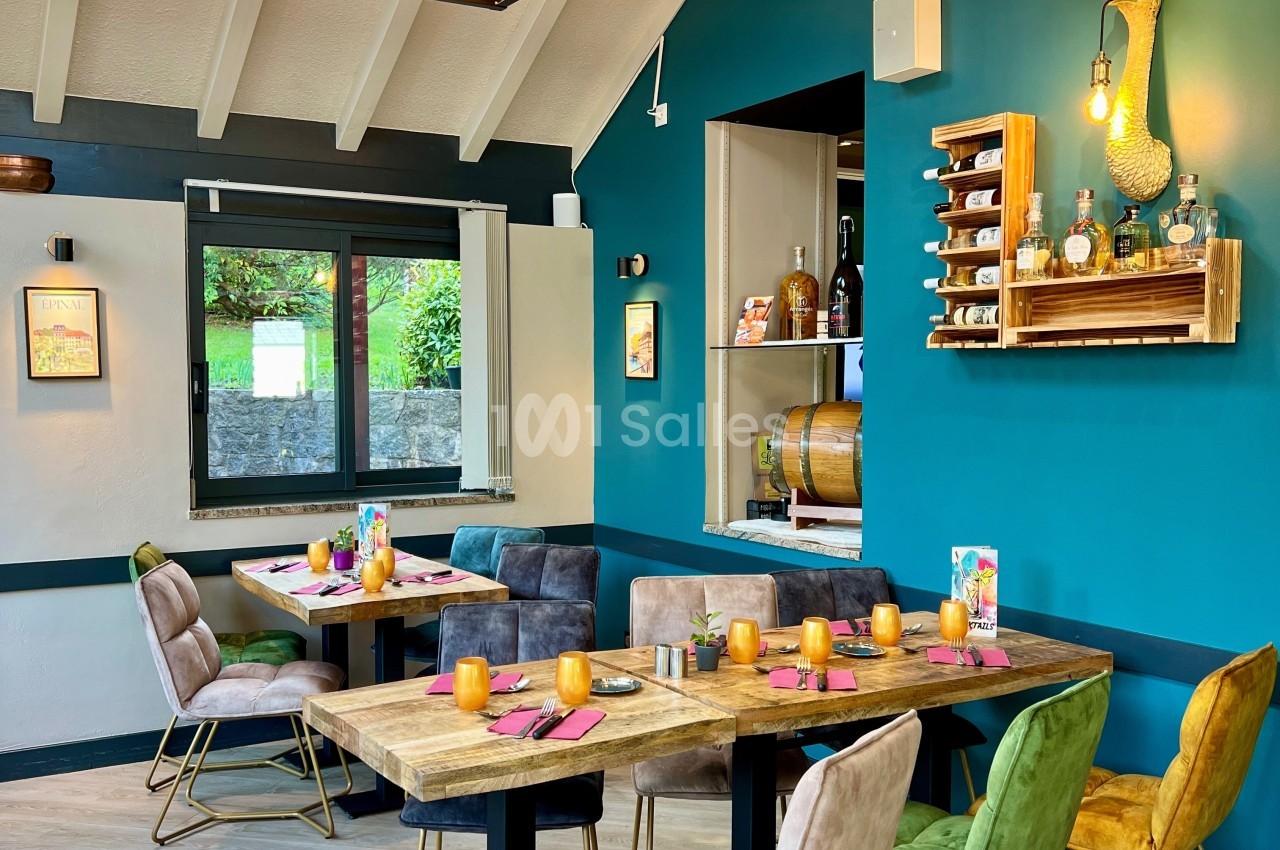 Salle de restaurant lumineuse avec tables en bois, chaises colorées et décoration murale chaleureuse.