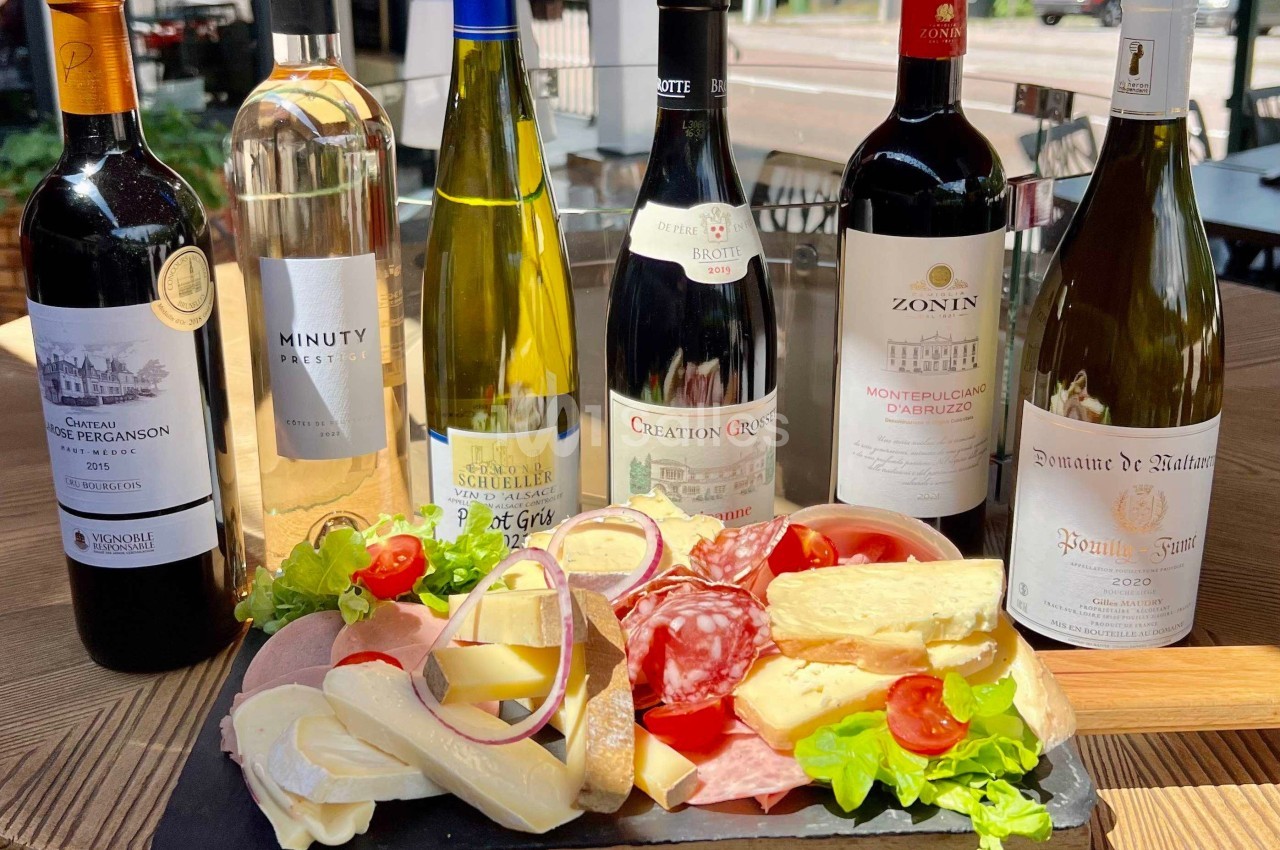 Plateau de charcuteries et fromages accompagné de six bouteilles de vin, disposé sur une table en bois.