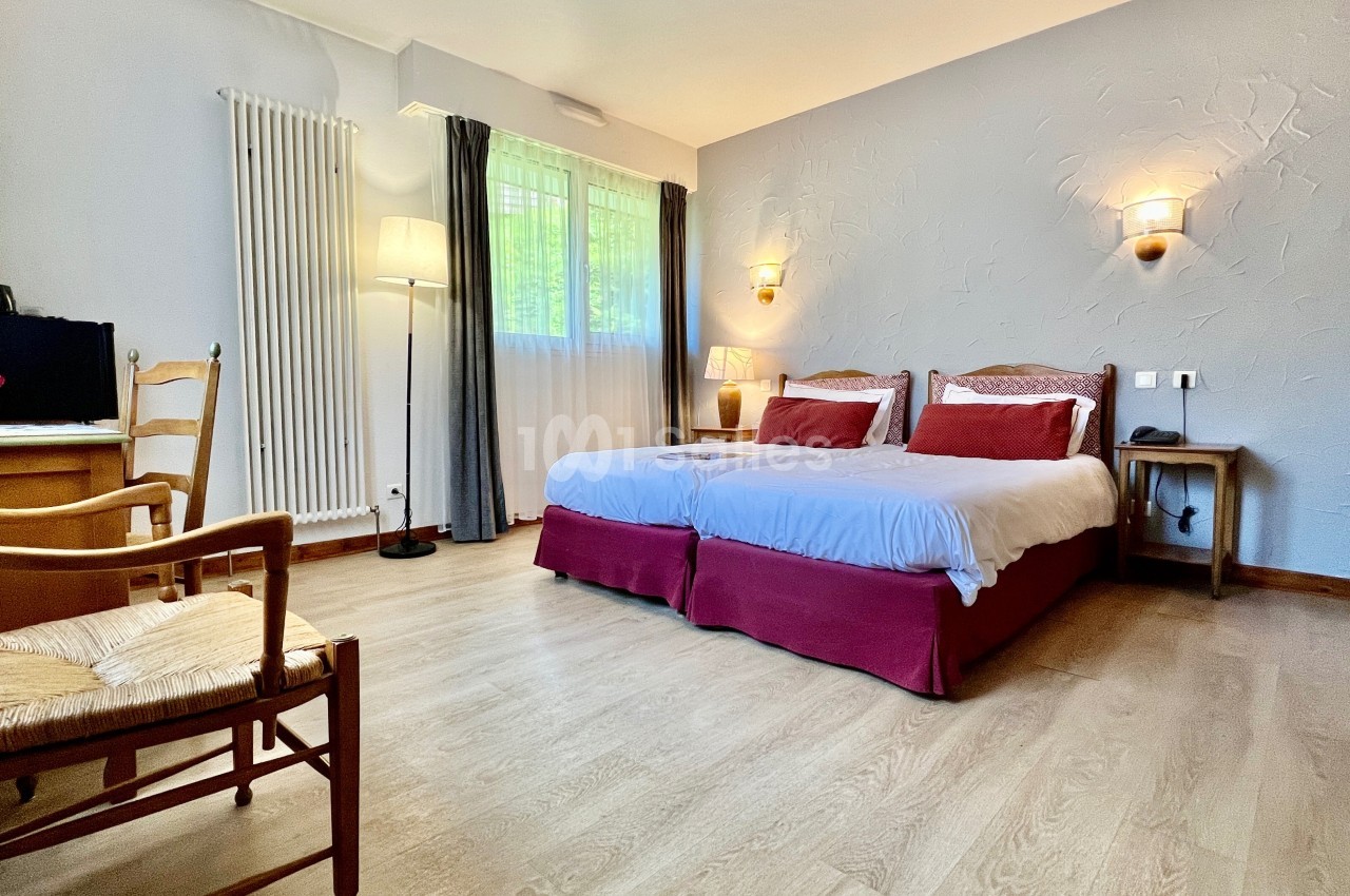 Chambre lumineuse avec deux lits simples, parquet clair, bureau, chaise en bois et fenêtre avec rideaux.