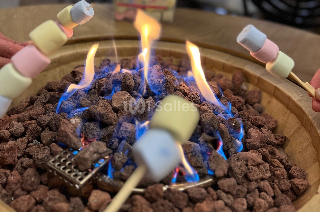 Des guimauves colorées sont grillées sur des brochettes au-dessus d'un feu de pierres volcaniques.