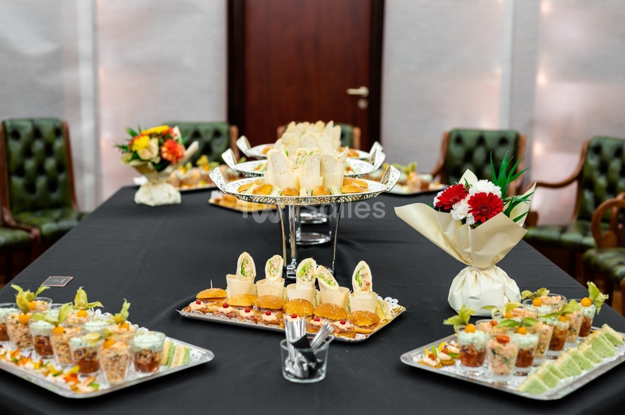 Buffet avec des amuse-bouches variés, disposés sur des plateaux élégants dans une salle avec des chaises en arrière-plan.