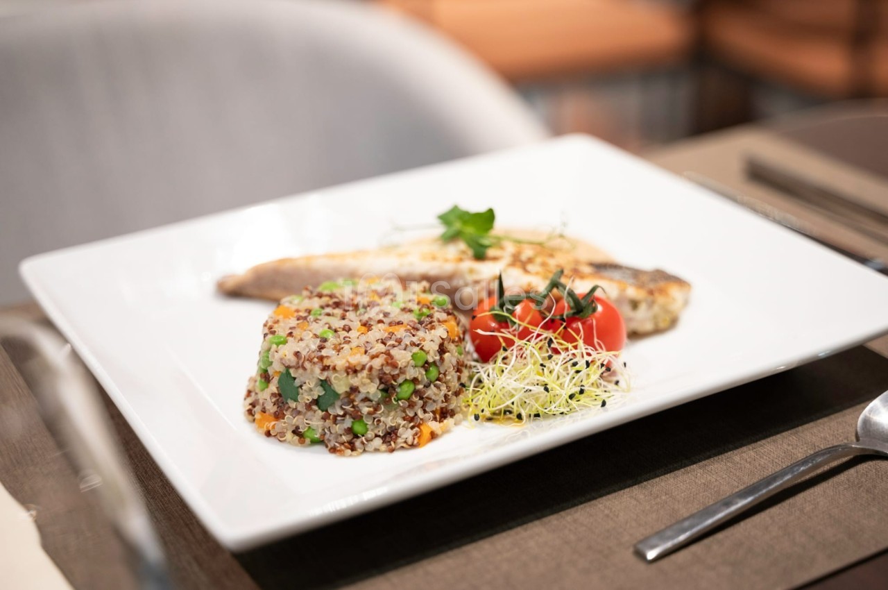 Assiette contenant du poisson grillé, un mélange de quinoa aux légumes, des tomates cerises et des pousses germées.