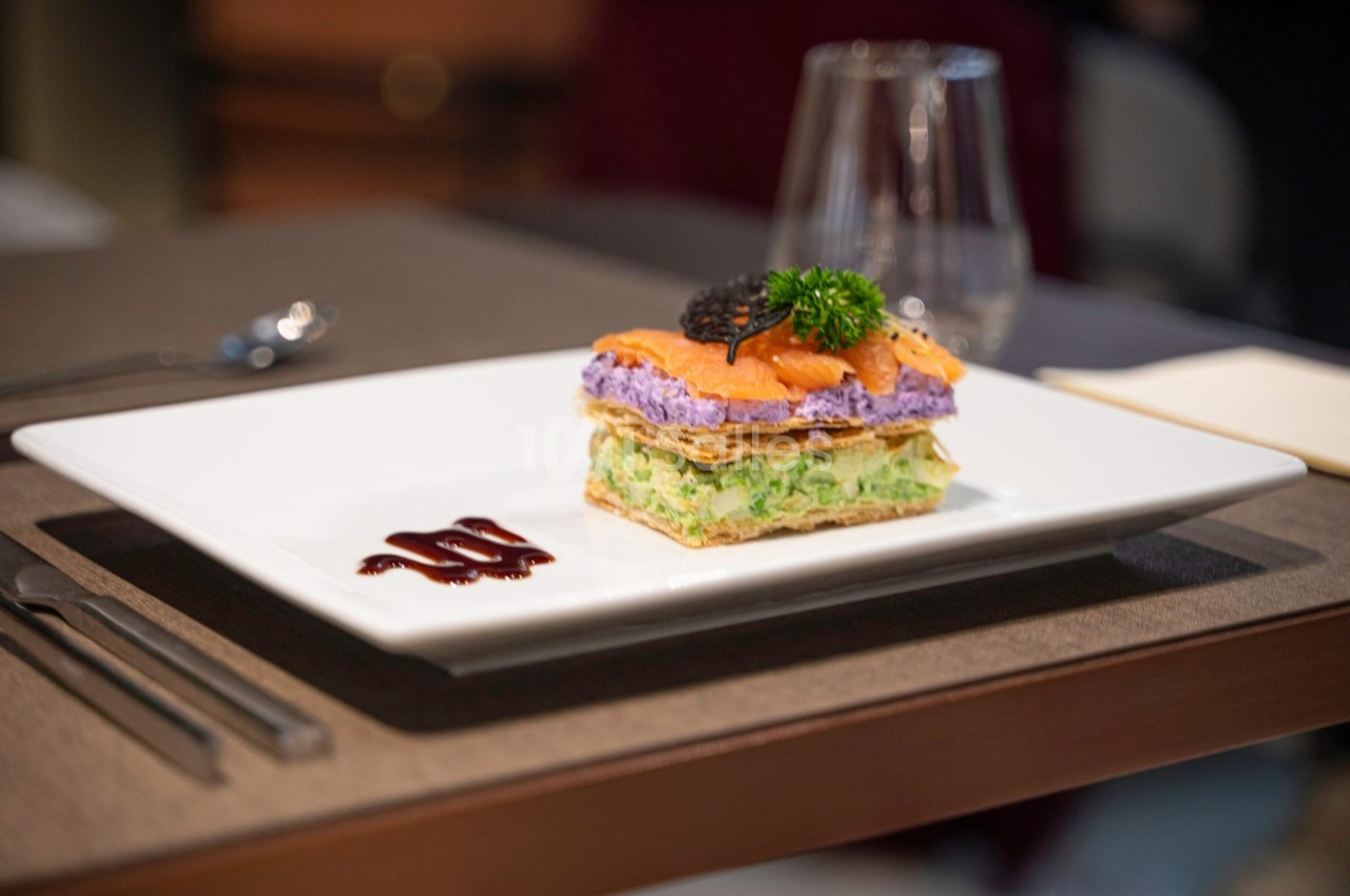 Millefeuille salé avec couches de légumes et saumon, décoré de caviar et d'herbes, servi sur une assiette blanche.
