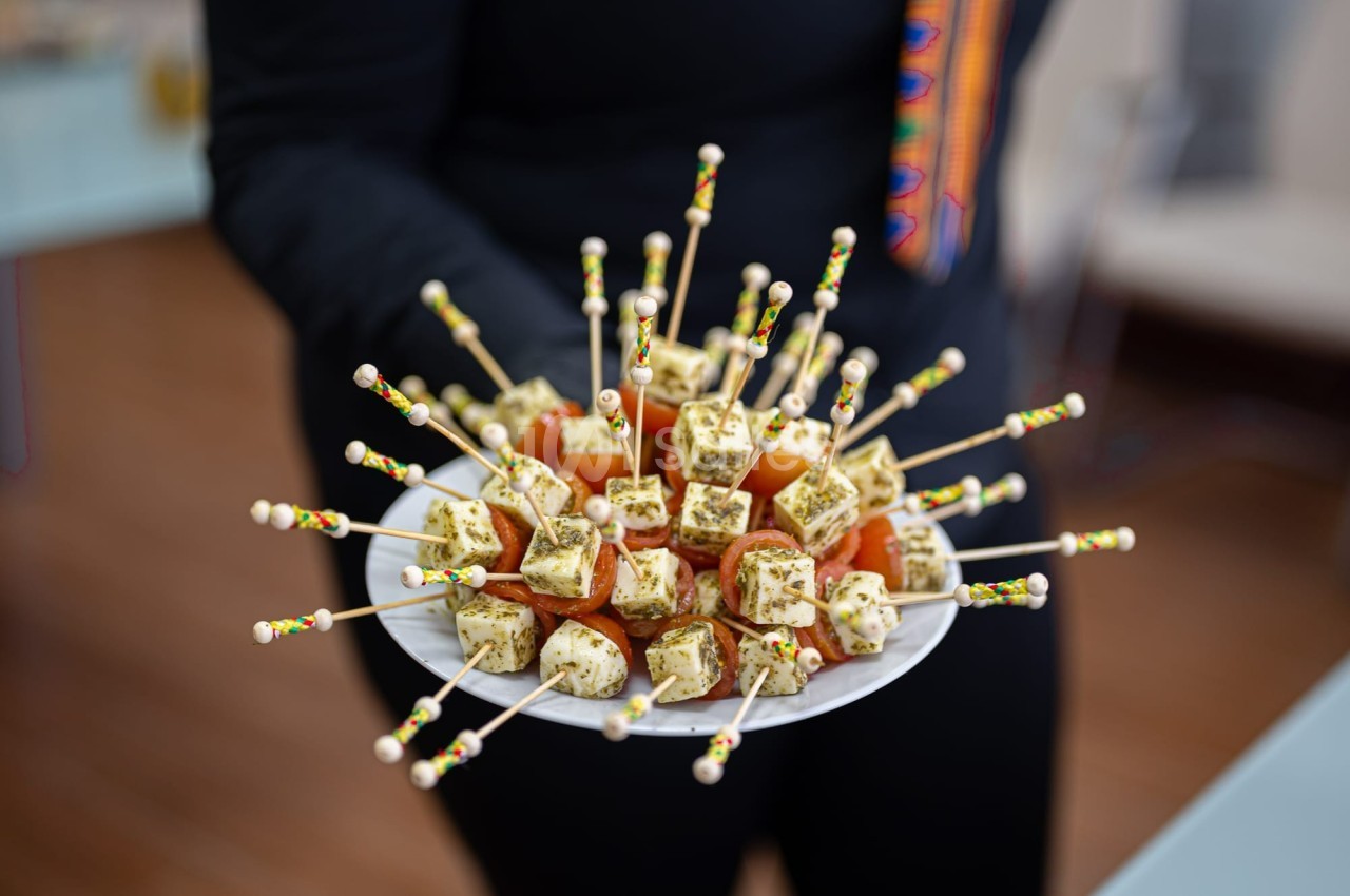 Assiette de brochettes apéritives avec cubes de fromage aux herbes et tomates cerises, tenue par une personne.