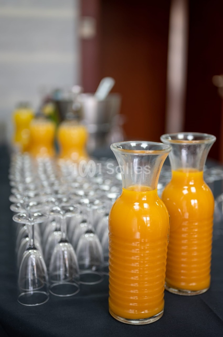 Carafes de jus d'orange posées sur une table noire, entourées de rangées de verres vides retournés.