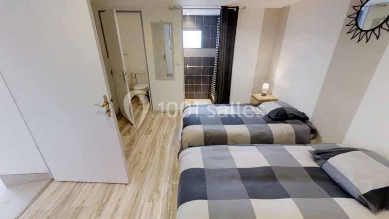 Chambre avec deux lits simples, sol en parquet clair, salle de bain attenante et décoration sobre.