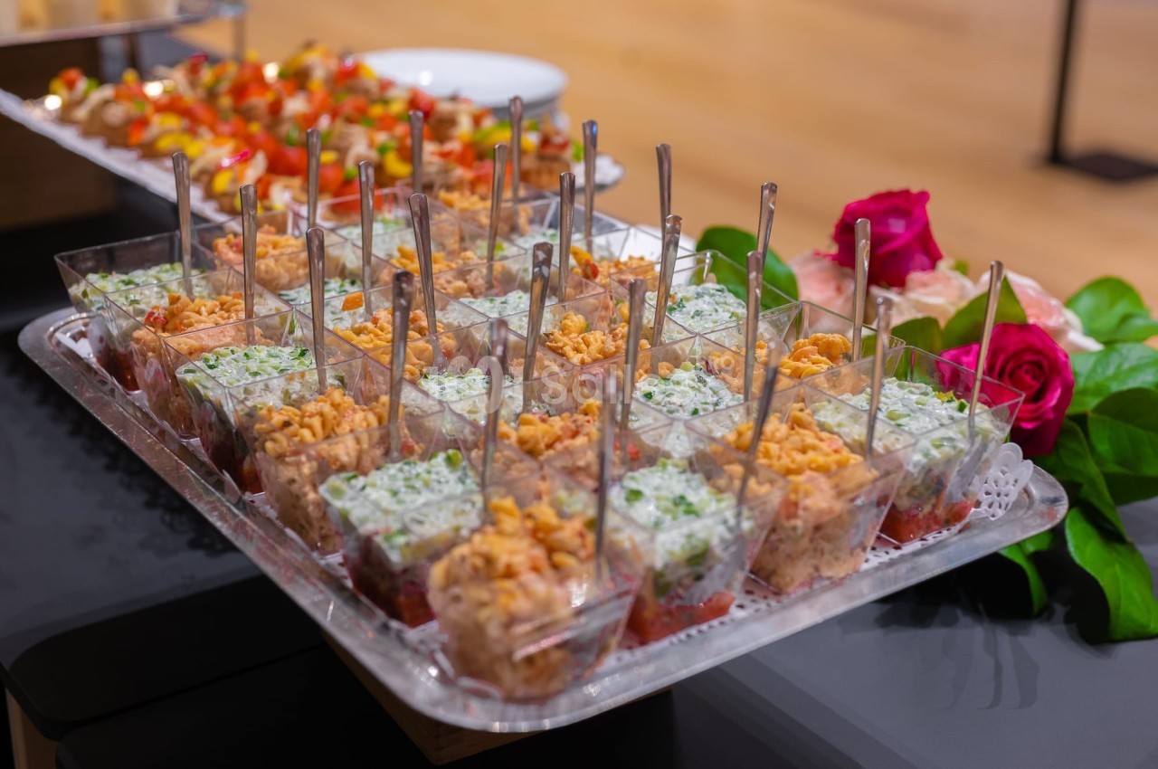 Plateau de verrines garnies de préparations salées variées, disposées avec des cuillères, décoré de roses.
