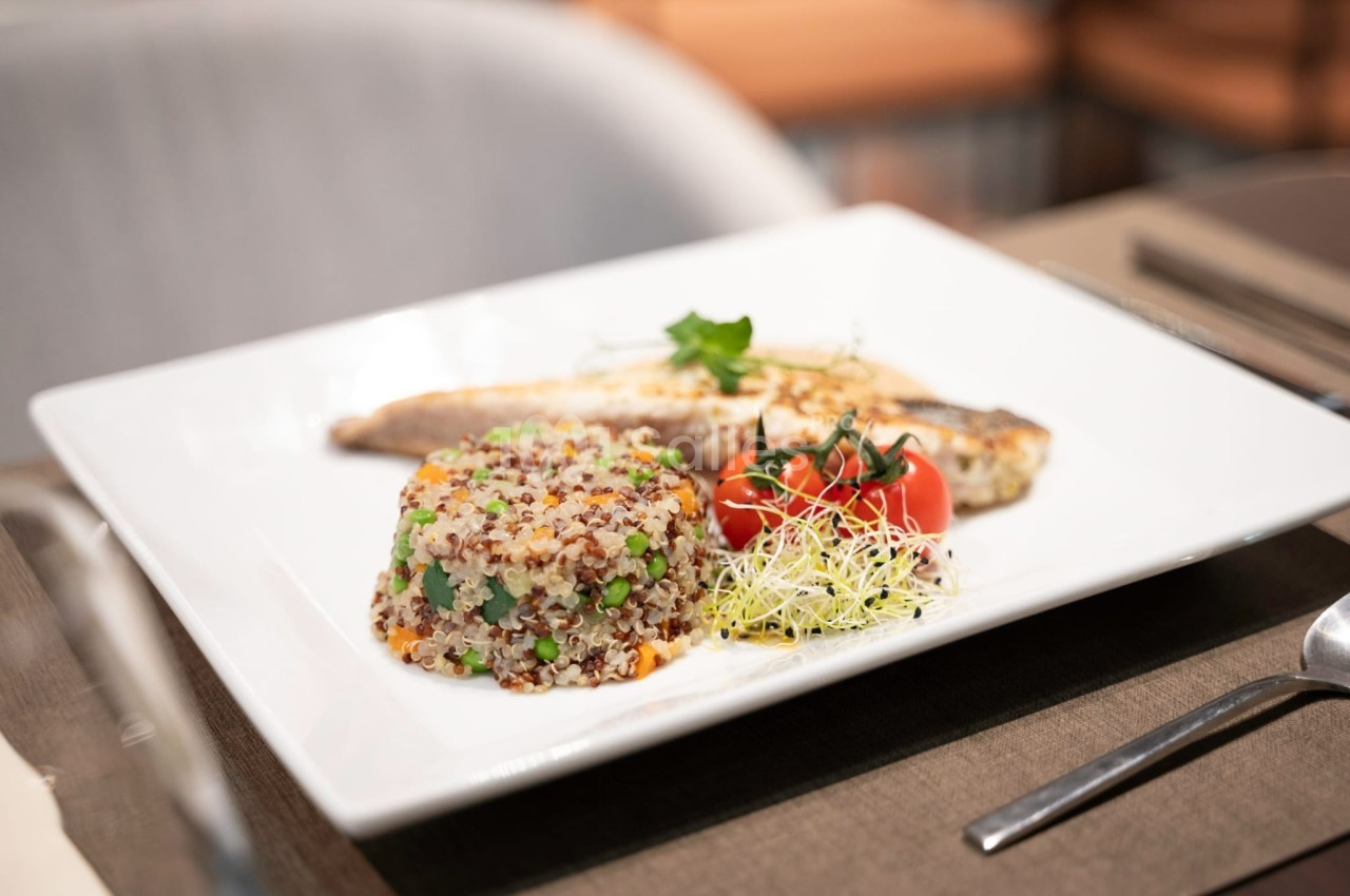 Assiette contenant du poisson grillé, un mélange de quinoa aux légumes, des tomates cerises et des pousses germées.
