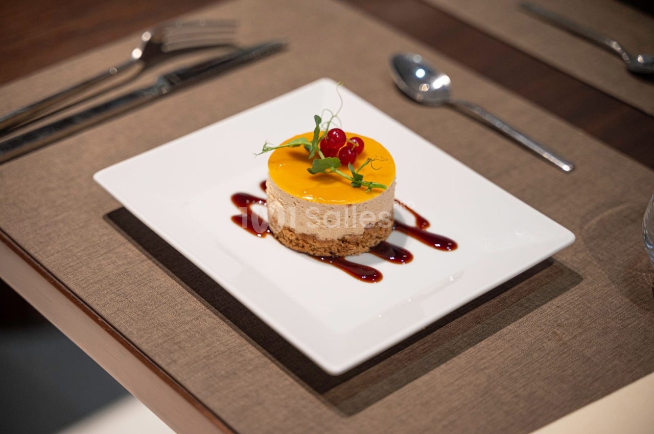 Dessert sur une assiette carrée, composé d'une base biscuitée, d'une mousse et d'un coulis, décoré de groseilles et de…