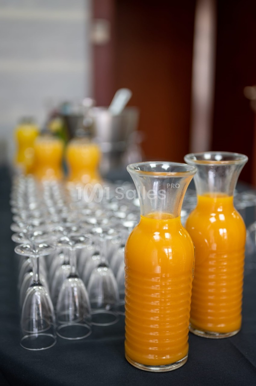 Carafes de jus d'orange posées sur une table noire, entourées de rangées de verres vides retournés.