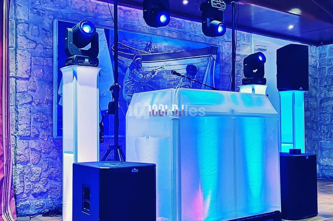 Installation de matériel de sonorisation et d'éclairage avec une table de DJ illuminée dans une salle en pierre.