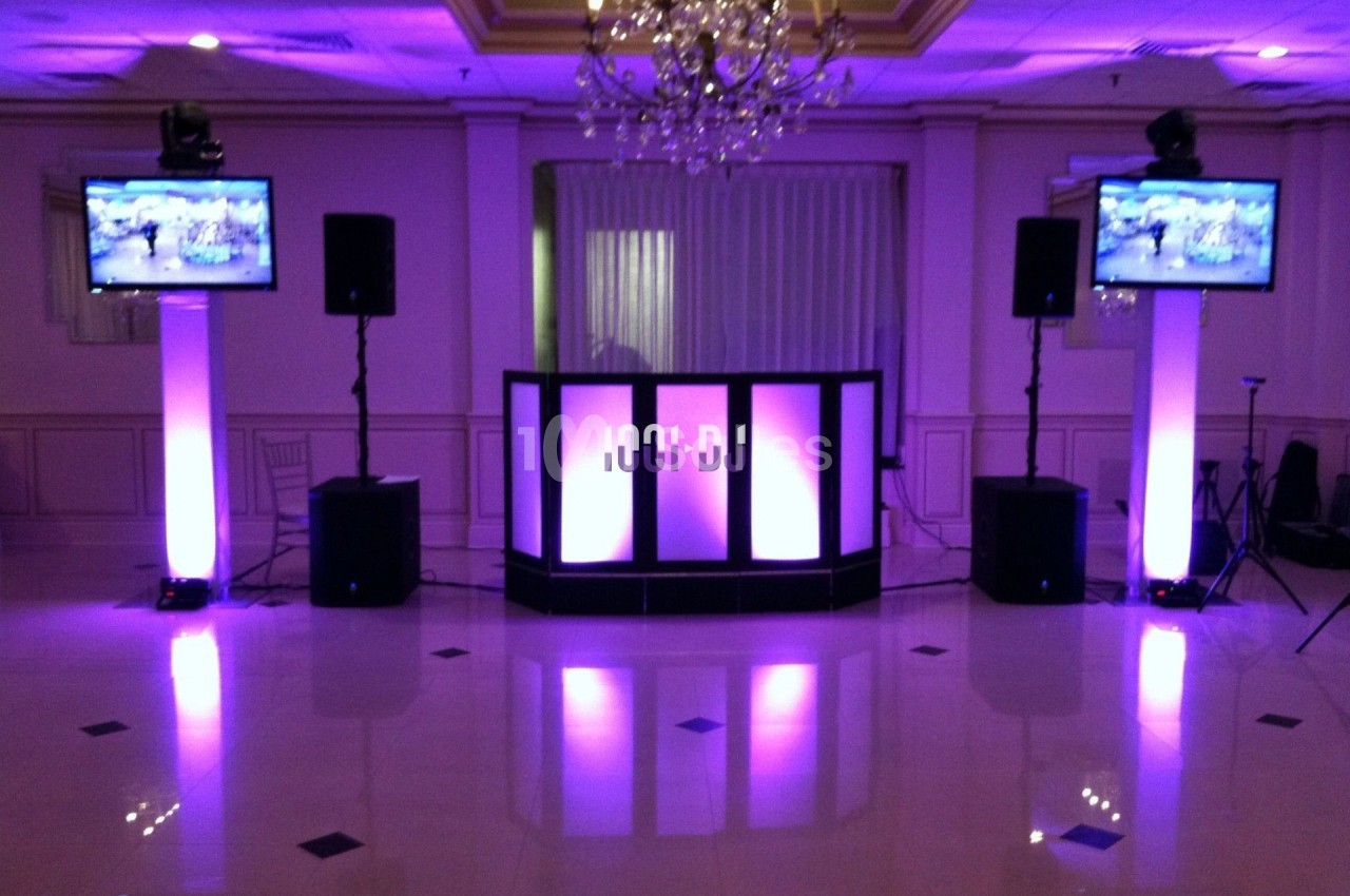 Installation de matériel audiovisuel avec éclairage violet, comprenant une table de mixage, haut-parleurs et écrans.