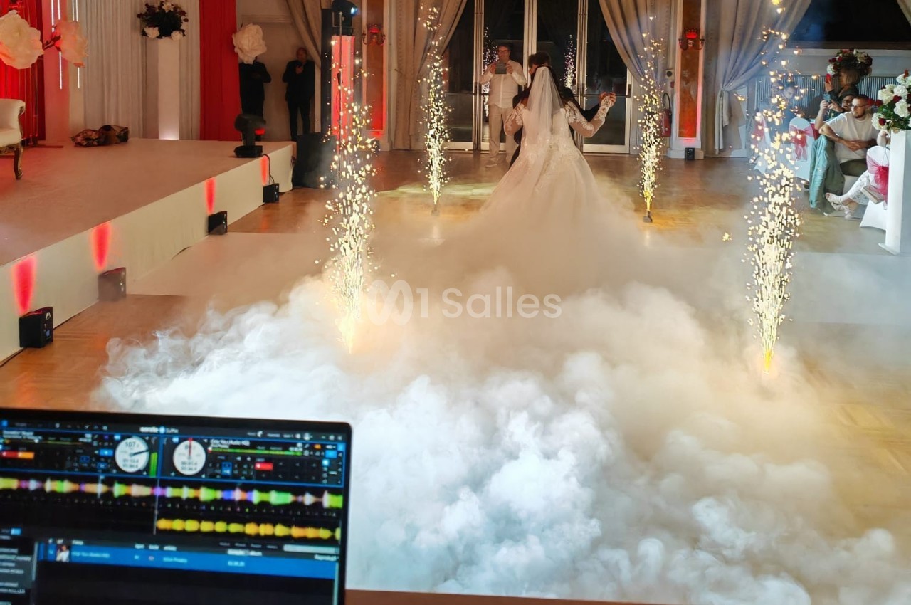 Un couple de mariés danse au milieu d'effets de fumée et d'étincelles dans une salle de réception décorée.