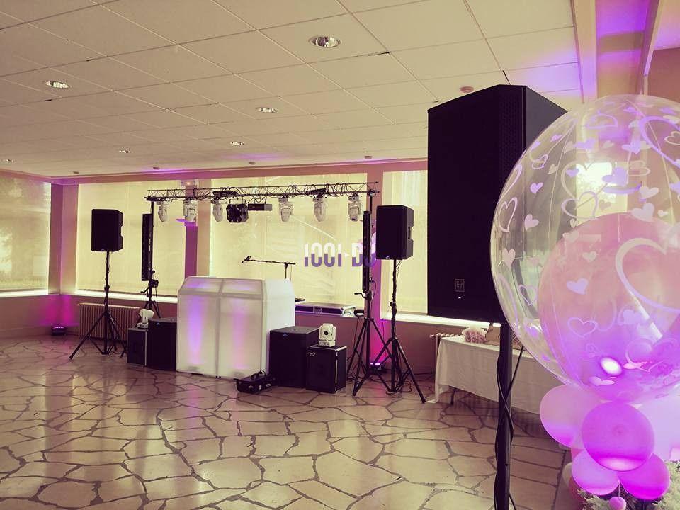 Salle décorée pour un événement avec éclairage violet, sono, pupitre de DJ et ballon transparent à motifs de cœurs.