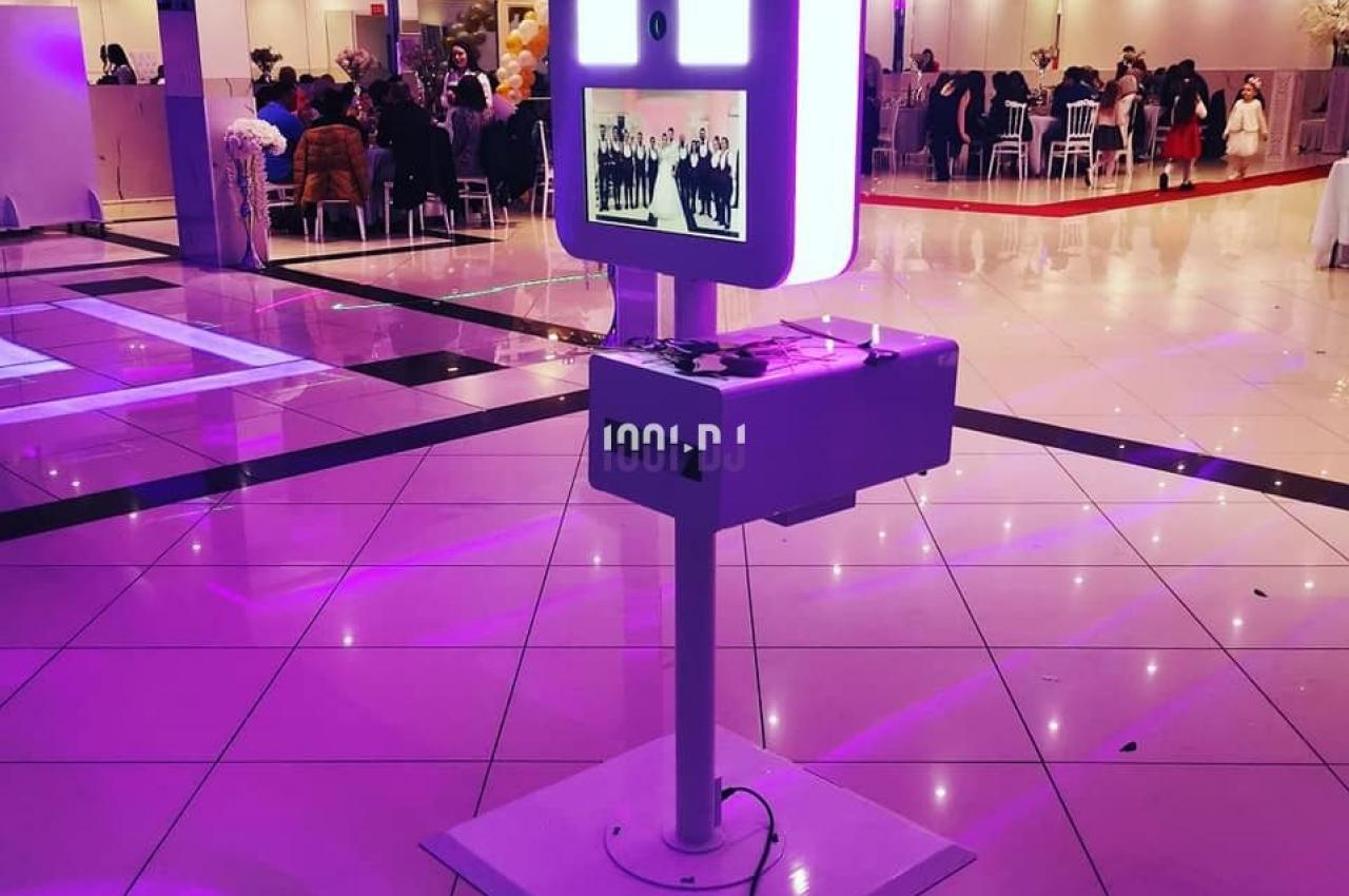 Borne photo interactive éclairée en violet dans une salle de réception avec des invités en arrière-plan.