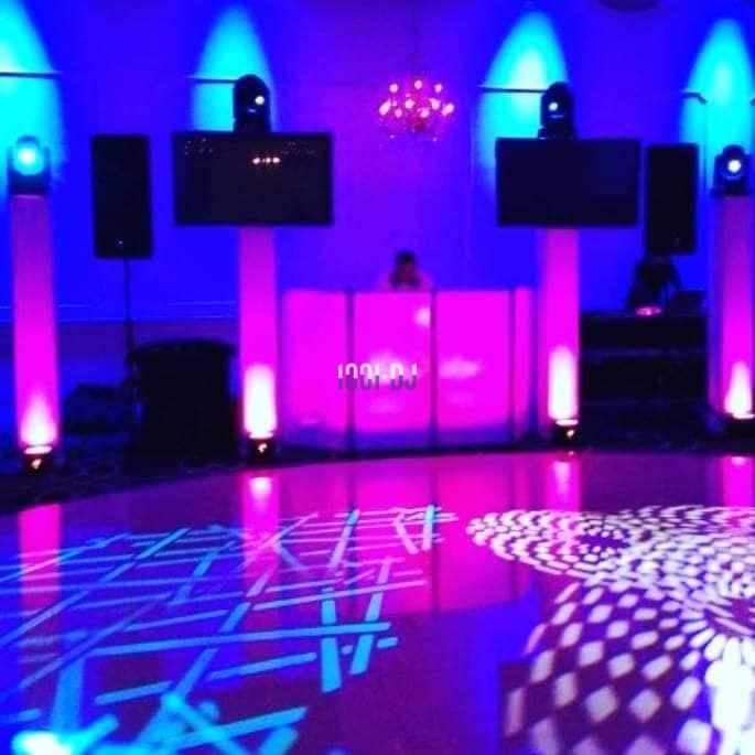 Salle de réception avec éclairage coloré, piste de danse illuminée et DJ derrière une console.
