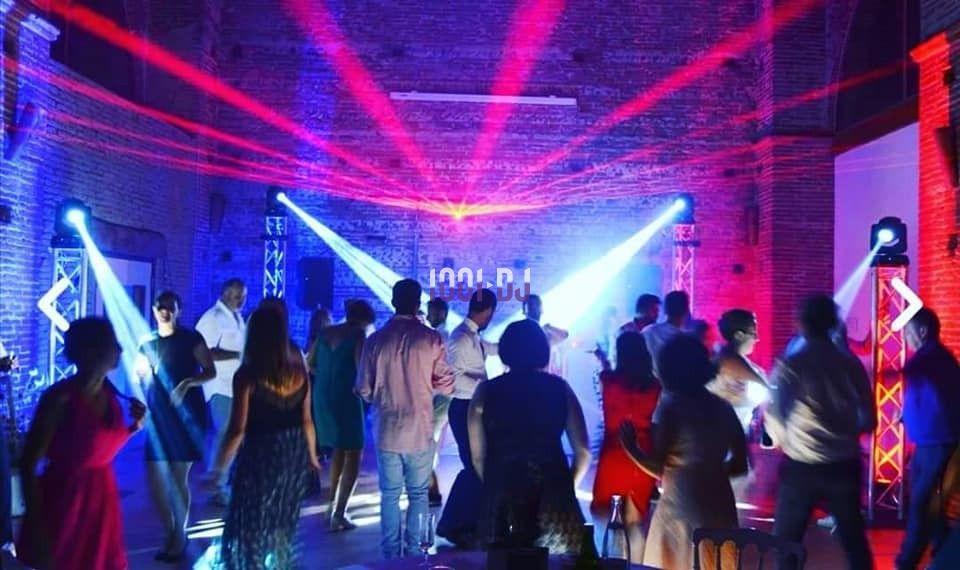 Des personnes dansent sous des jeux de lumières colorées dans une salle en briques lors d'une soirée festive.