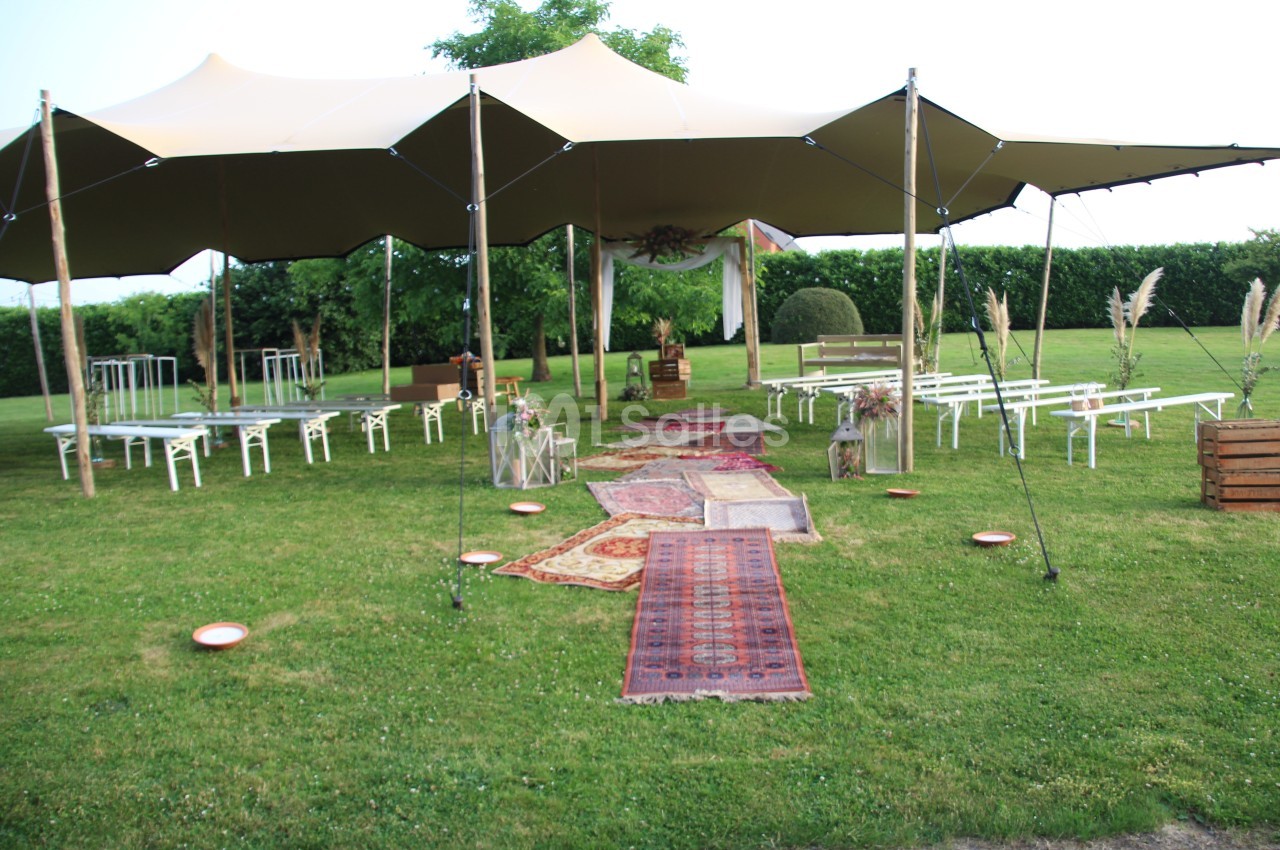 Tente beige installée dans un jardin, avec allée de tapis colorés menant à un espace de cérémonie décoré.
