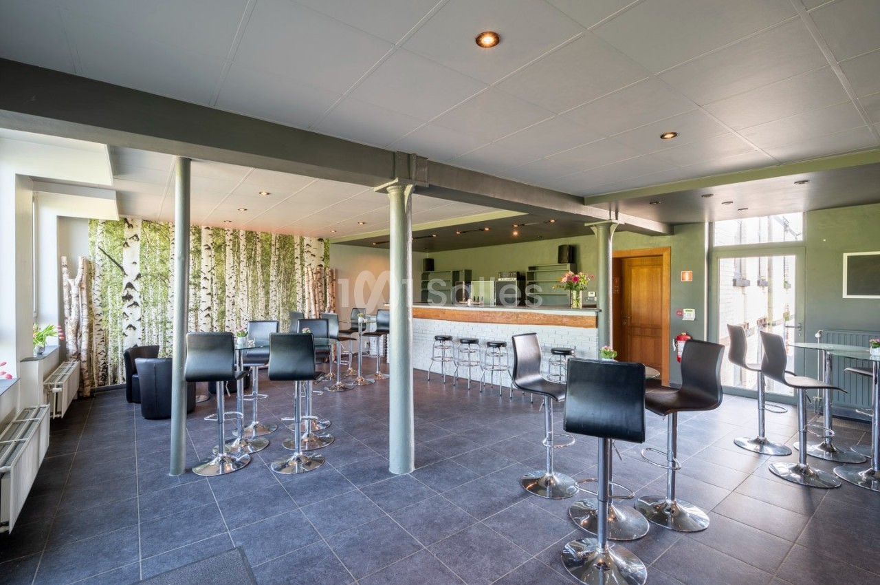 Salle moderne avec tables hautes, chaises noires et bar en bois clair, décorée de panneaux imitant des troncs de bouleaux.