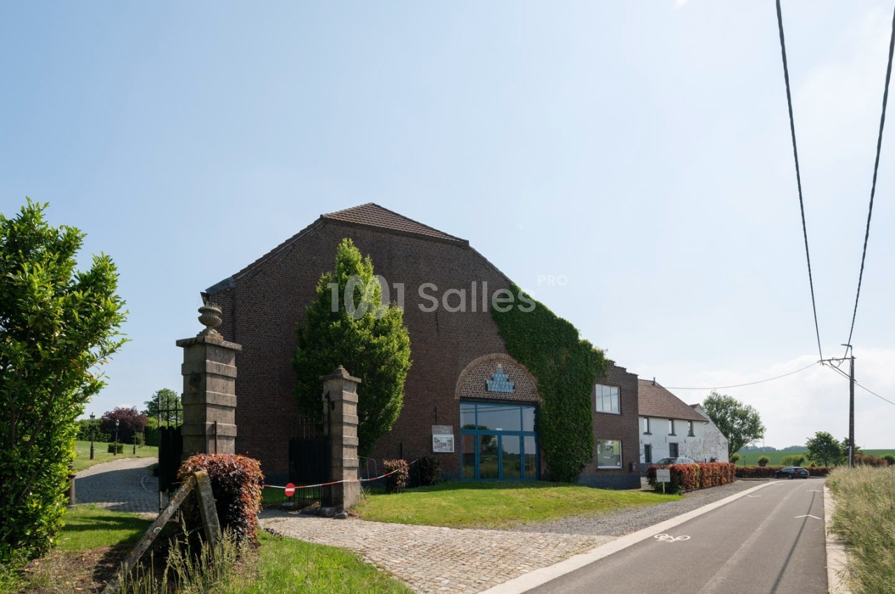 Bâtiment en briques avec façade partiellement couverte de lierre, situé au bord d'une route de campagne.