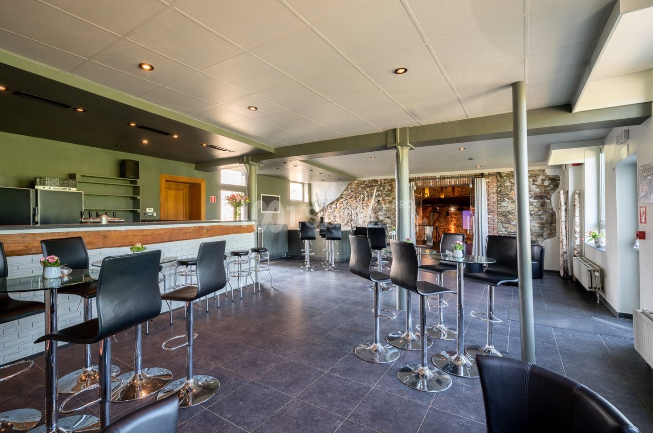 Salle moderne avec comptoir de bar, chaises hautes noires, murs en pierre et éclairage encastré.