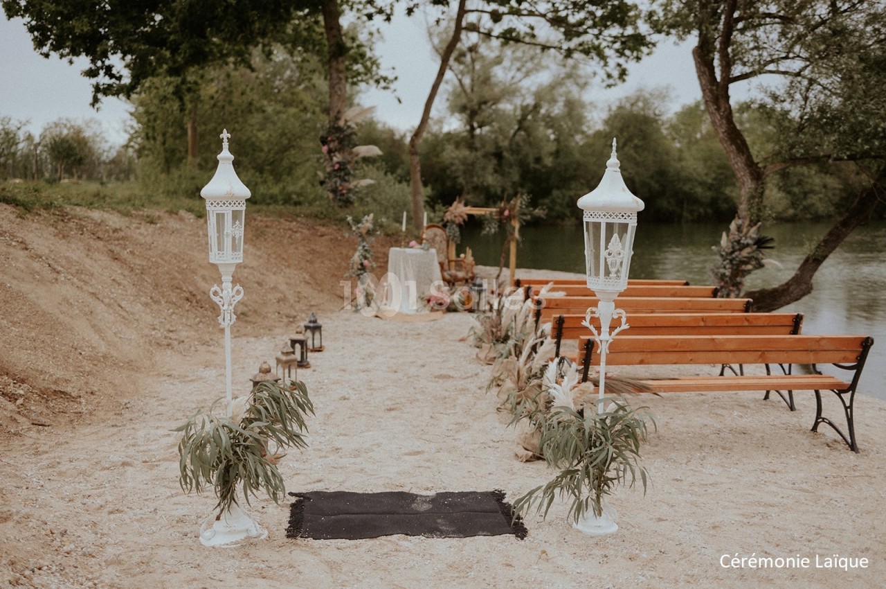 Allée décorée avec des lanternes blanches menant à un autel en plein air, entourée de bancs en bois et de verdure.