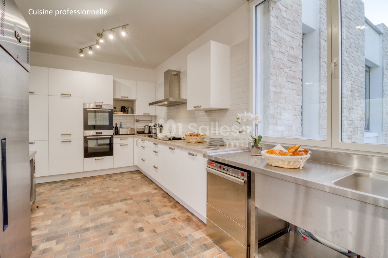 Cuisine moderne avec équipements professionnels, plan de travail en inox, four encastré et sol en carrelage.