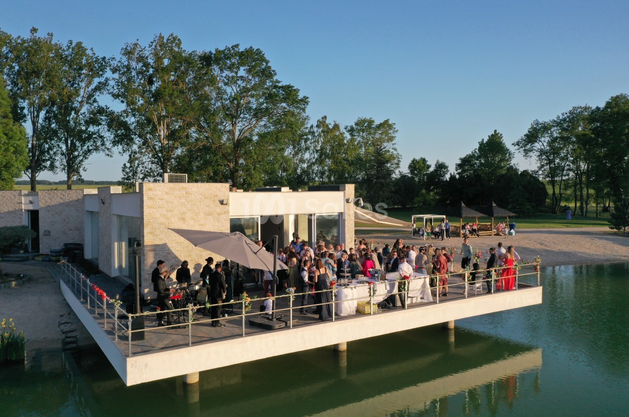 Groupe de personnes rassemblées sur une terrasse au bord d'un plan d'eau, entourée de verdure par temps ensoleillé.