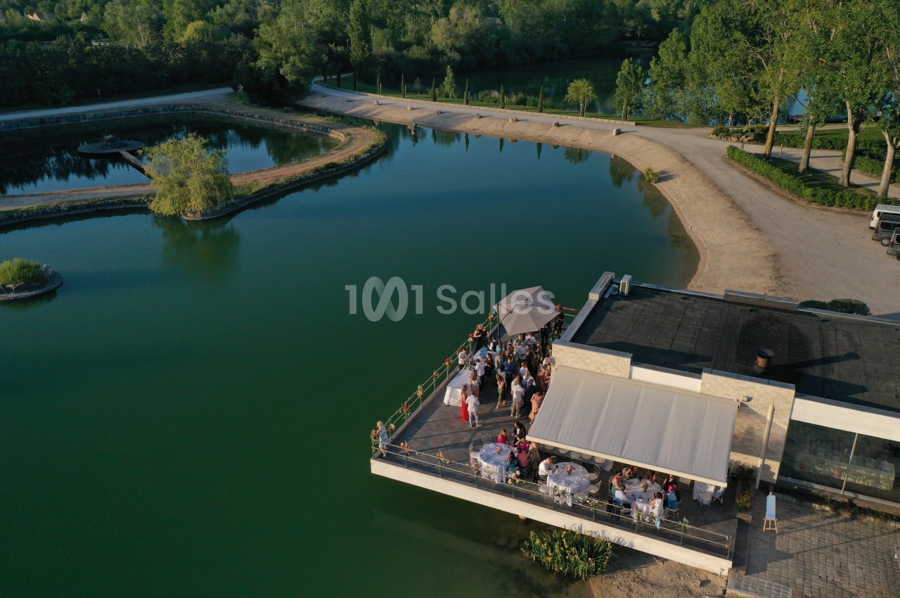 Terrasse d'un bâtiment au bord d'un lac, occupée par des convives lors d'un événement en plein air.