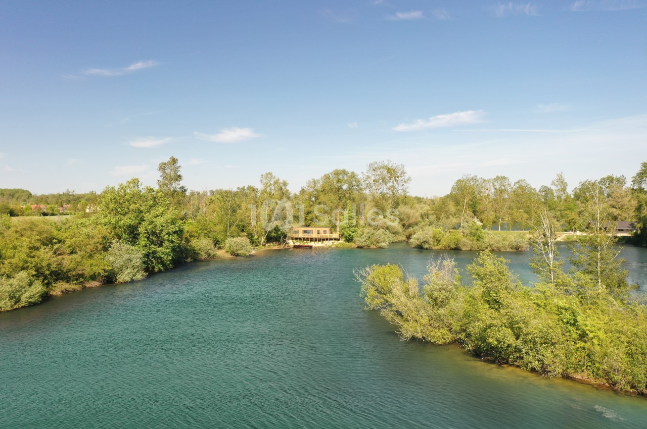 Vue aérienne d'un lac entouré de végétation dense avec une petite maison en bois au bord de l'eau.