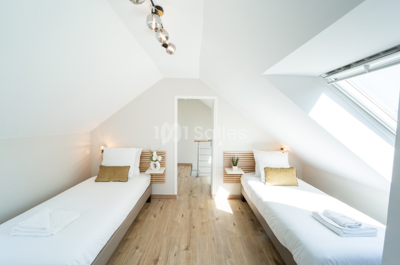 Chambre lumineuse avec deux lits simples, parquet au sol, fenêtre de toit et décoration minimaliste.