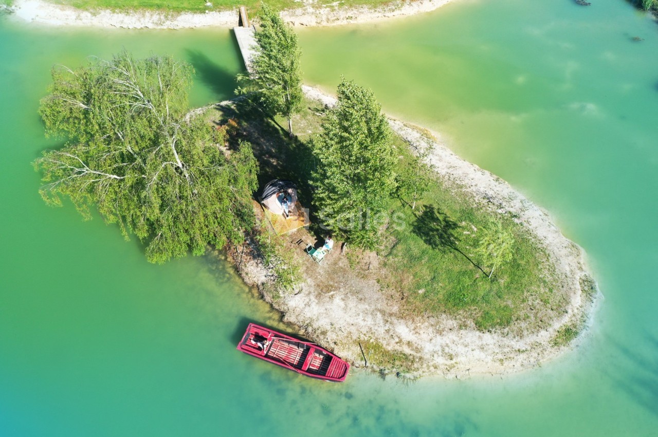 Vue aérienne d'une petite île verdoyante avec un bateau rouge amarré et un ponton en bois sur un lac turquoise.
