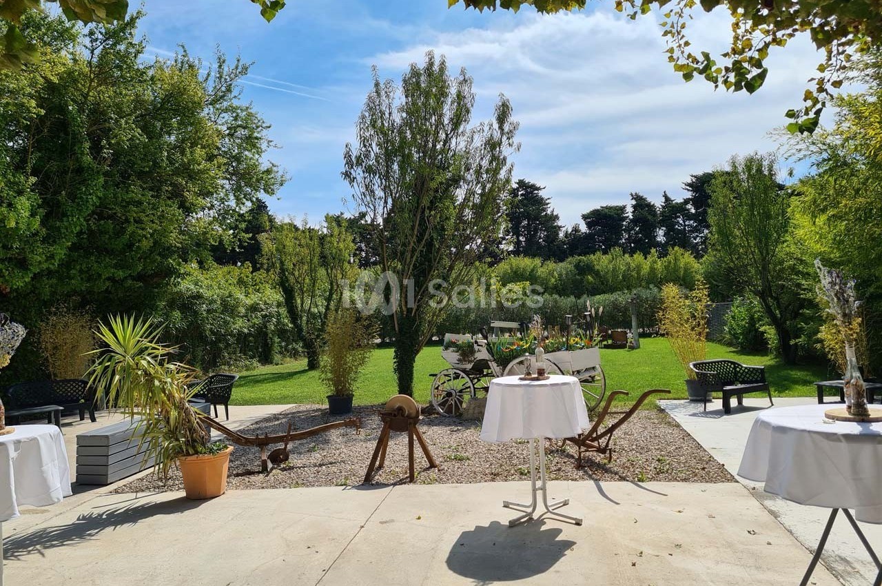 Jardin verdoyant avec tables et décorations rustiques, entouré d'arbres et de végétation sous un ciel dégagé.