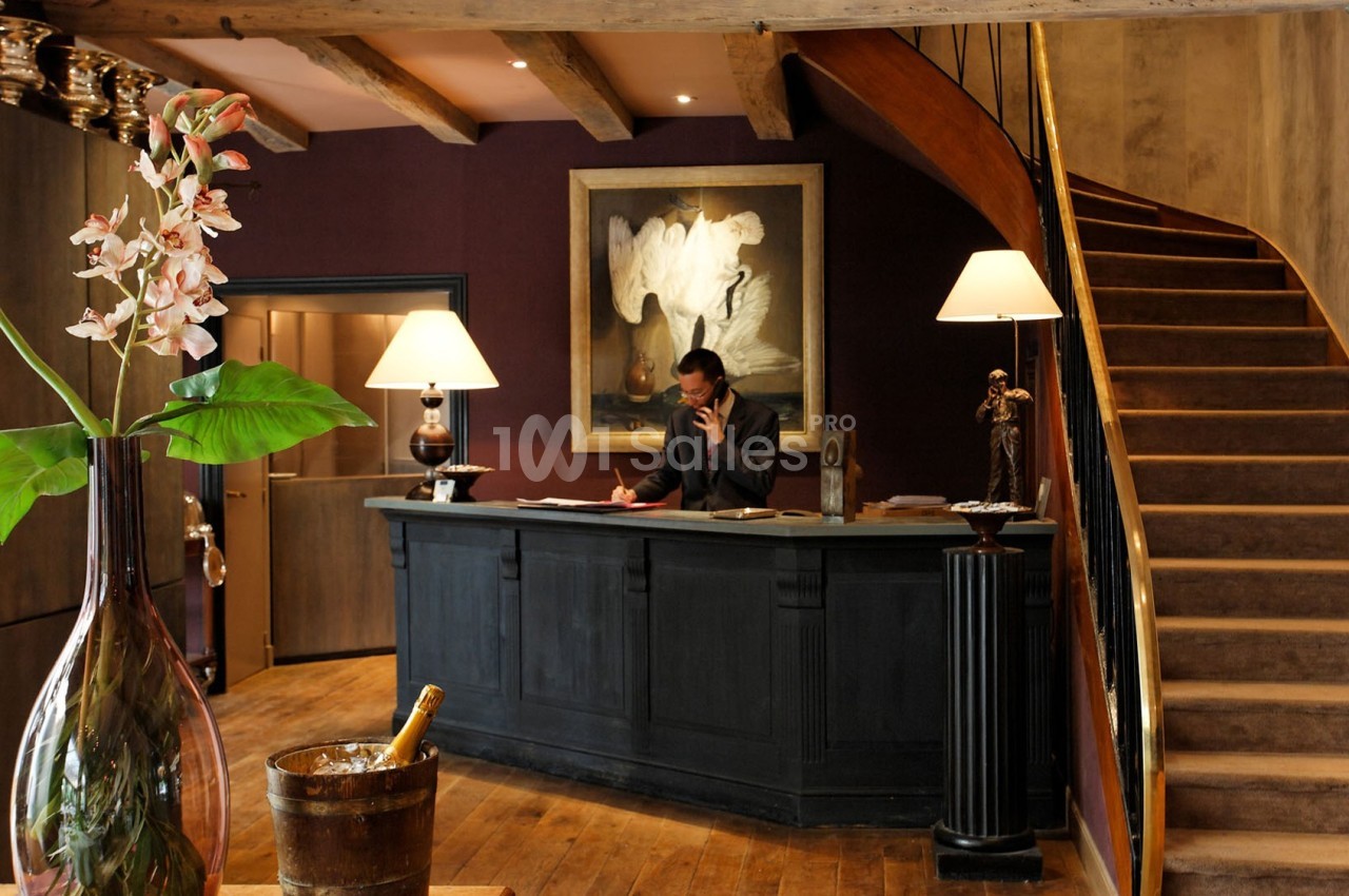 Accueil d'un hôtel avec un comptoir en bois, un réceptionniste, un escalier en colimaçon et une décoration élégante.