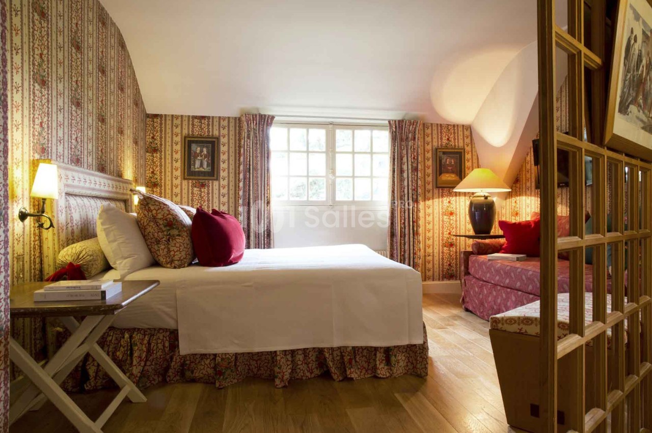 Chambre avec lit double, décorée de motifs floraux, éclairée par une fenêtre et des lampes, parquet au sol.