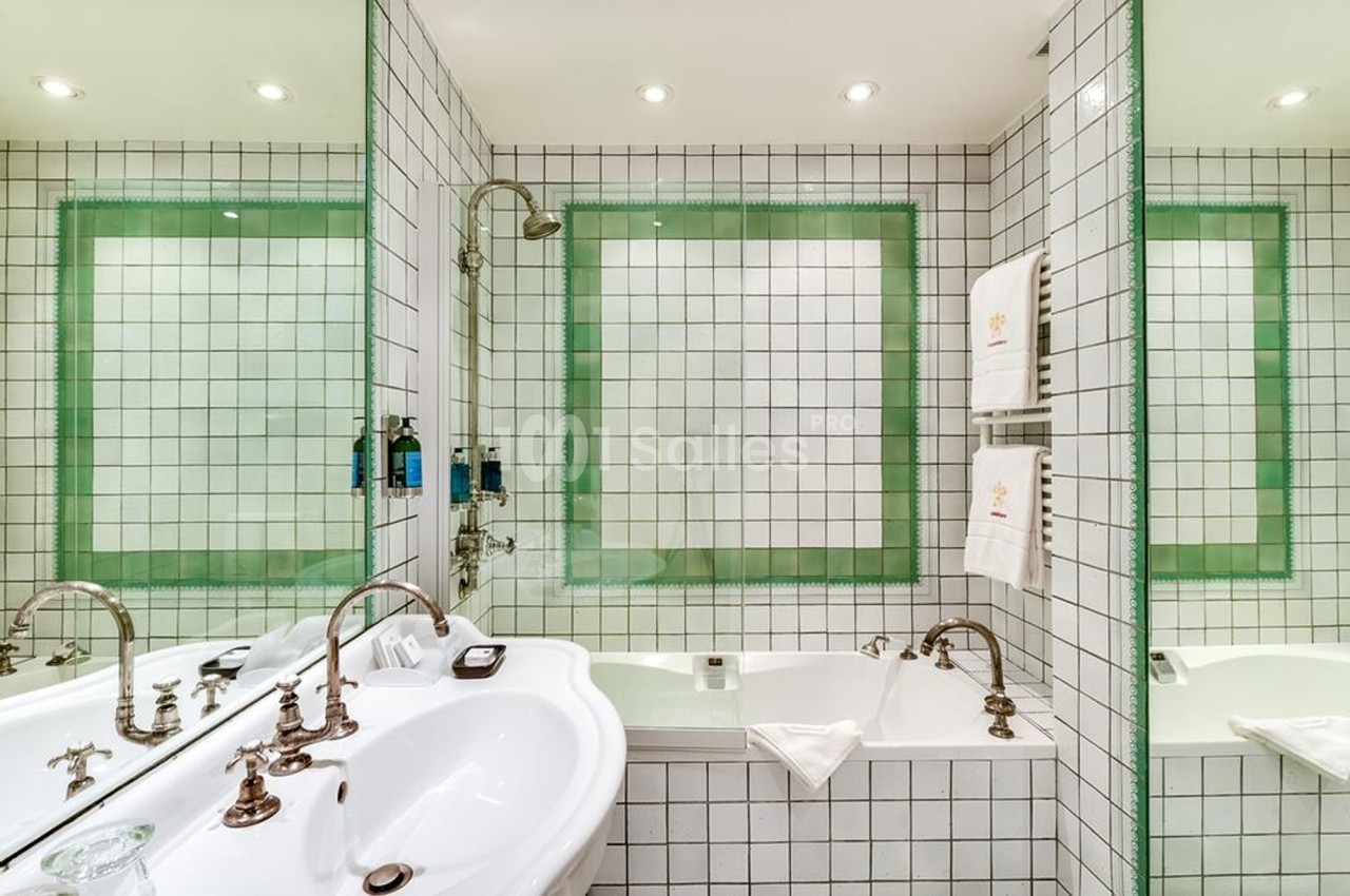 Salle de bain avec carrelage blanc, baignoire, double vasque, miroirs et éclairage encastré.