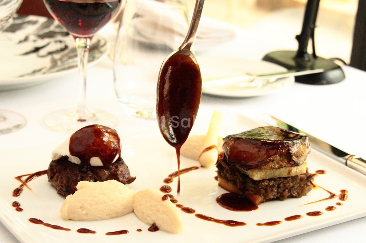 Assiette gastronomique avec viande, purée et sauce, servie sur une table dressée avec verre de vin et couverts.